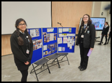 two girls stand smiling next to a board