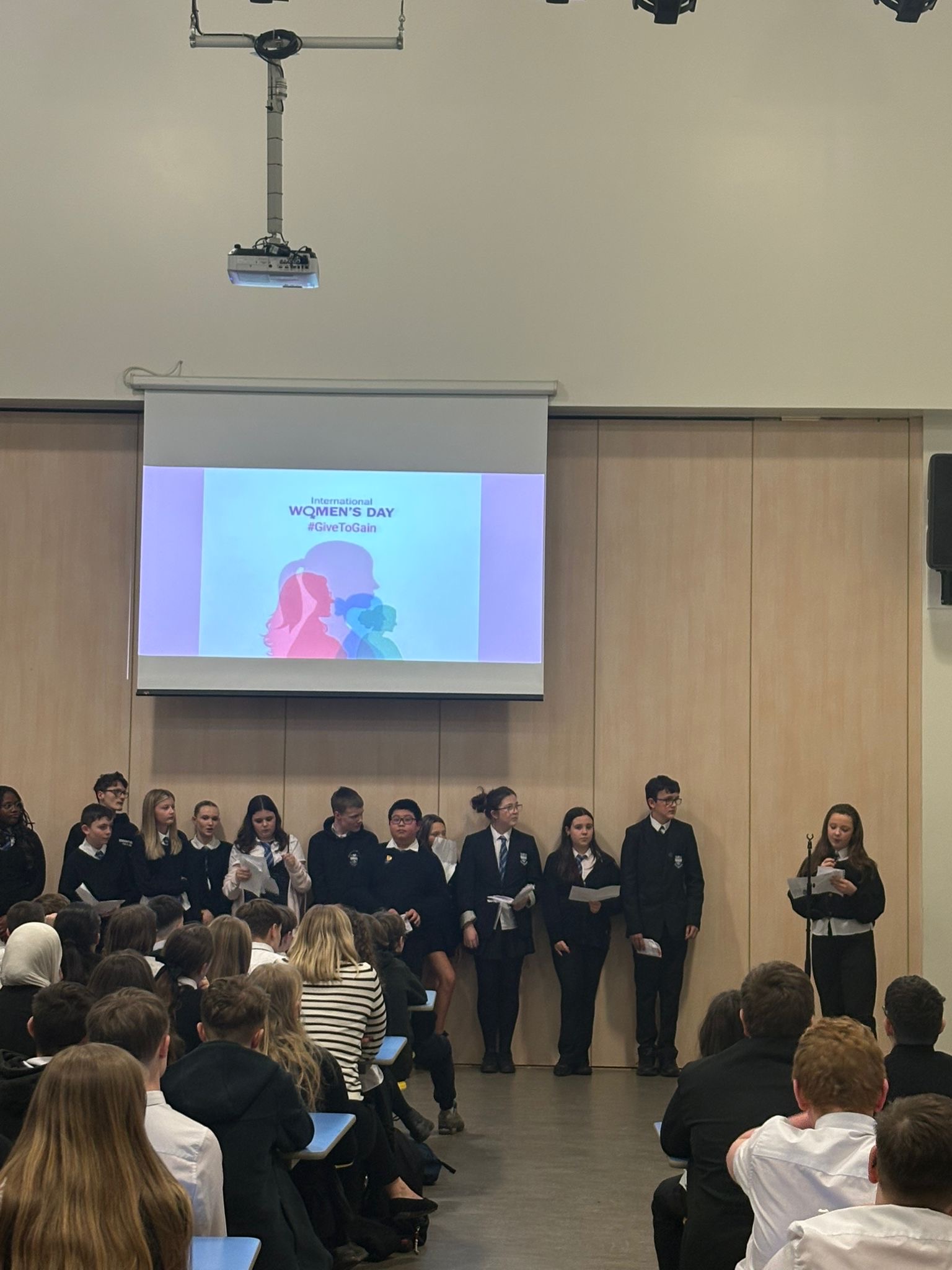 Pupils at assembly with a girl talking to the class