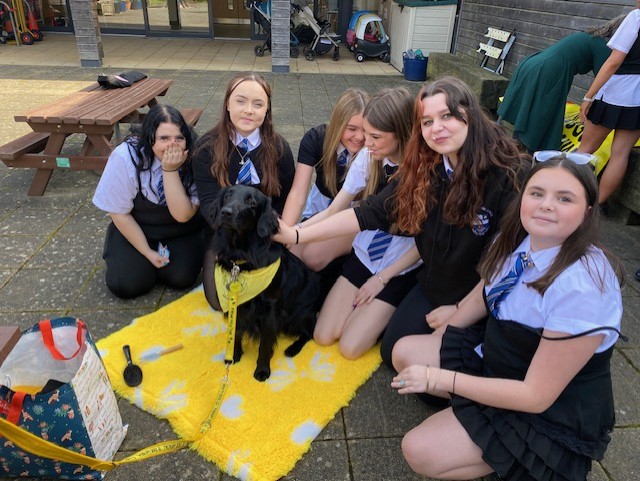 group of girls smile next to a black Labrador