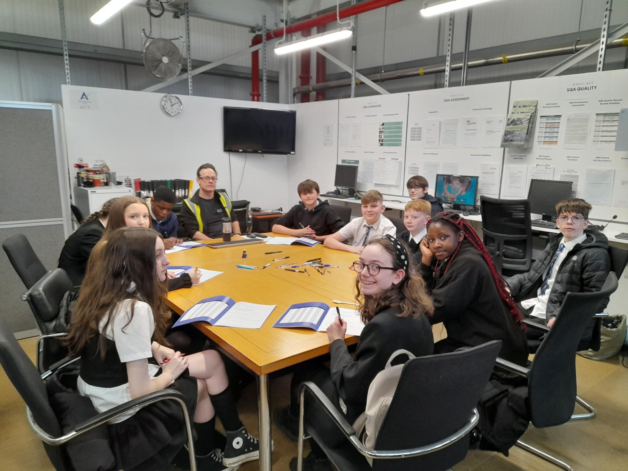 ppupils sat around a desk looking at the camera