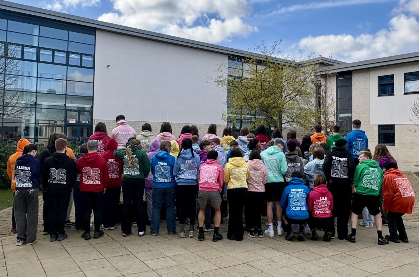 Group photo of school leavers wearing different coloured leavers hoodies with their backs turned to the camera