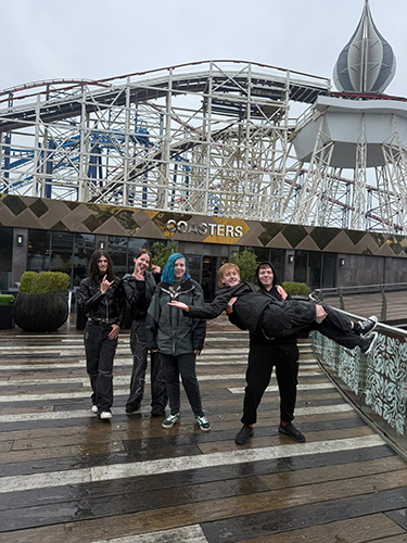 A group of boys teenagers standing in front of the rollercoasters