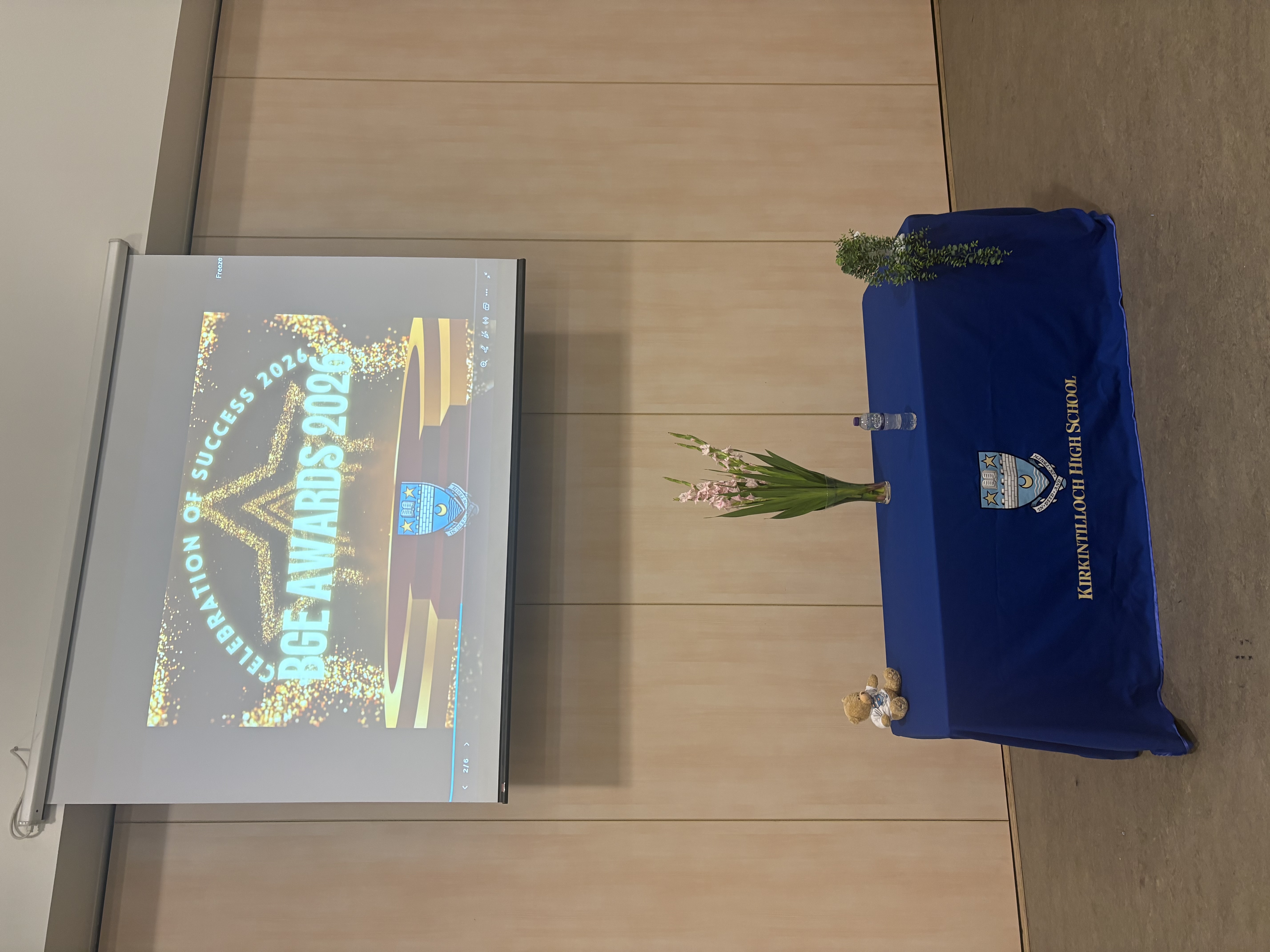table with a blue table cloth over it with the kirkintilloch high logo on it with a projector screen on the wall in the background