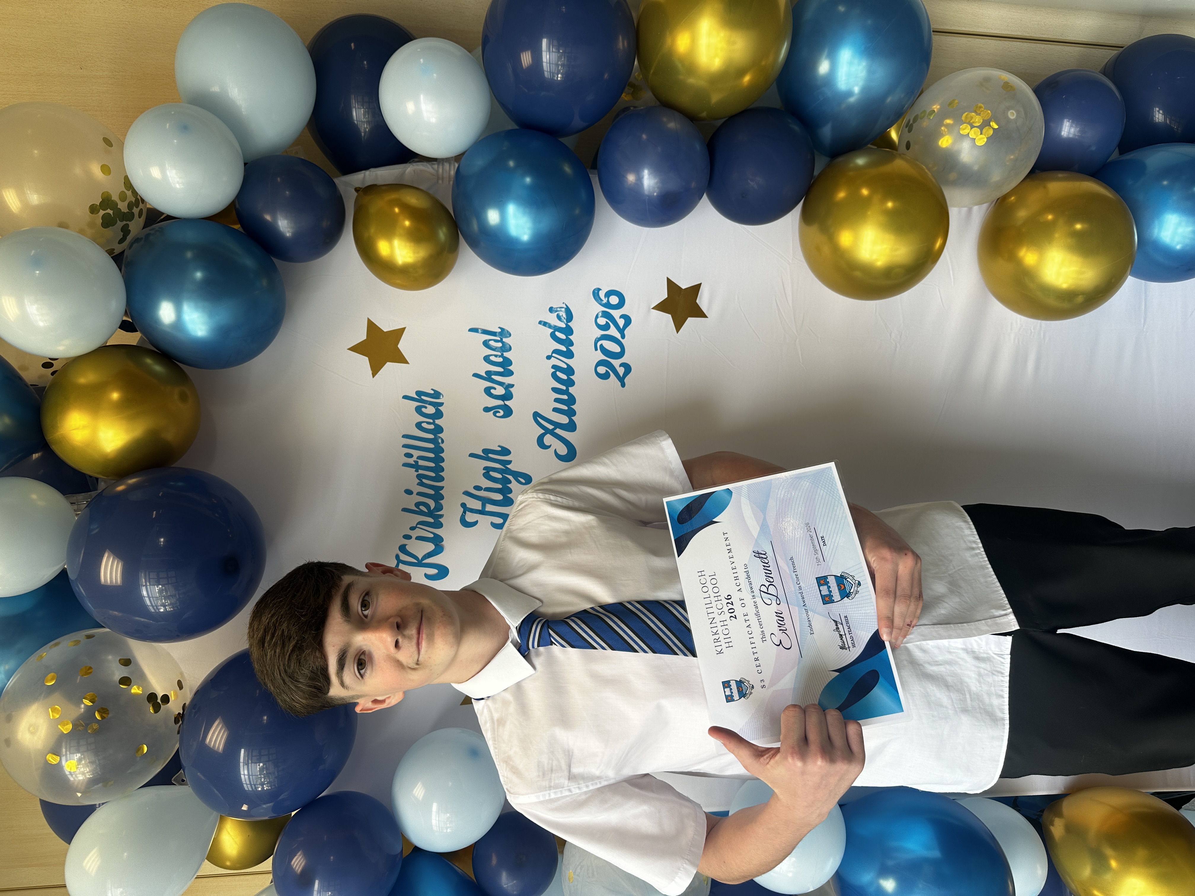 pupil holding a certificate of achievement while giving a thumbs up gesture